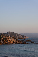 Sardinian coastline at dawn. Calm sea, rocky shore, and distant hills.