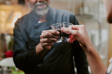 Medium close up of unrecognizable male hands clinking shot glasses full of coffee liquor