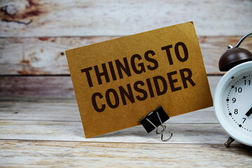 Things to consider text on paper card with alarm clock on wooden background