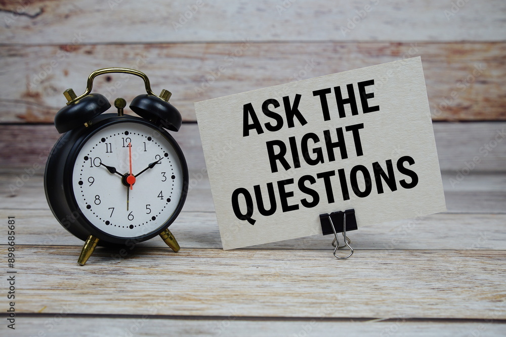 Poster ask the right questions text on paper card with alarm clock on wooden background