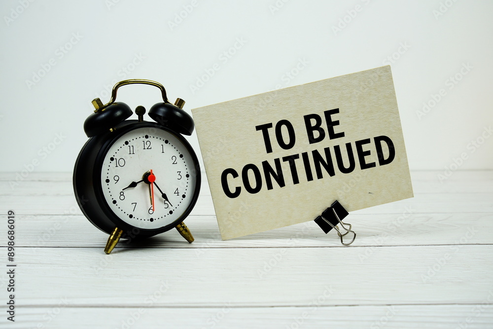 Poster to be continued text on paper card with alarm clock on wooden background