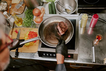Top view shot of unrecognizable male hands checking beef steak with crust on frying pan