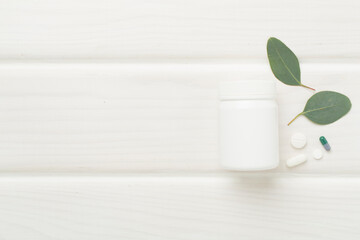Bottle with pills and green leaves on wooden background, top view