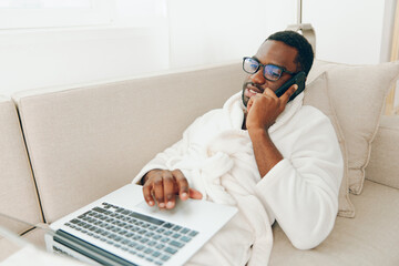 Smiling African American Man Working on Laptop in Home Office, Talking on Phone