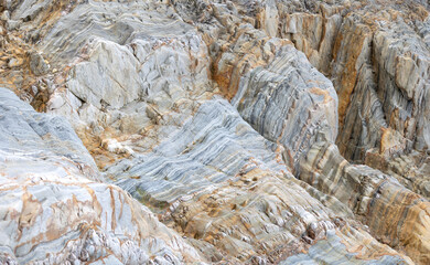 Layered rock formations featuring gray and orange hues with intricate geological textures and...
