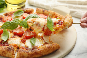 Woman taking piece of delicious Margherita pizza at white marble table, closeup