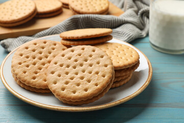 Tasty sandwich cookies and glass of milk on light blue wooden table, closeup