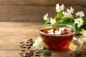 Hot jasmine tea in cup and flowers on wooden table, space for text