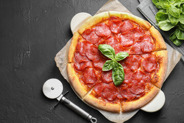 Tasty pepperoni pizza, cutter and basil on black textured table, flat lay. Space for text