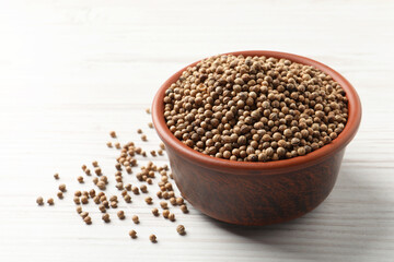 Dried coriander seeds in bowl on wooden table