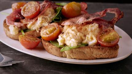 Scrambled egg and bacon on toasted bread with tomatoes and spinach.
