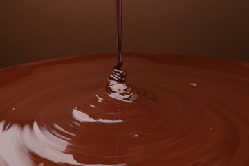 Pouring delicious melted chocolate on brown background, closeup
