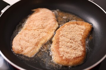 Schnitzels cooking in frying pan on stove, closeup