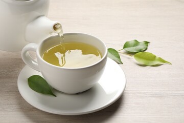 Pouring refreshing green tea into cup at wooden table, closeup