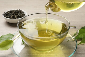 Pouring refreshing green tea into cup at wooden table, closeup