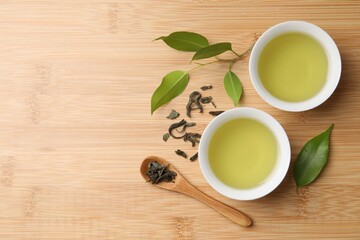 Refreshing green tea in cups, spoon and leaves on wooden table, flat lay. Space for text