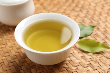 Refreshing green tea in cup and leaves on table, closeup