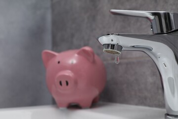 Water saving concept. Piggy bank and water drop flowing from tap in bathroom, selective focus