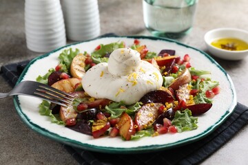 Plate with fresh burrata salad on grey textured table, closeup