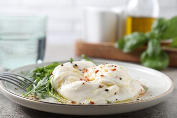 Delicious burrata cheese, arugula and spices on grey table, closeup