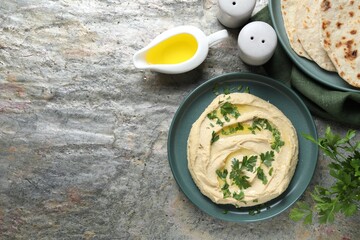 Delicious hummus with olive oil, pita and parsley on grey textured table, flat lay. Space for text