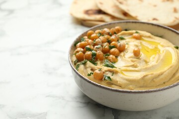 Delicious hummus with olive oil, chickpeas and parsley in bowl on white marble table, closeup. Space for text