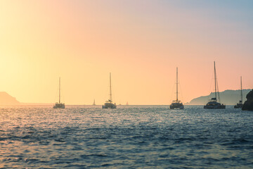 Golden hour casts a magical glow over the Aegean Sea, painting the sky in hues of pink and orange. Silhouetted boats gently bob on the water, creating a serene and idyllic scene near Santorini