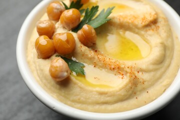 Delicious hummus with olive oil, chickpeas and parsley in bowl on grey table, closeup