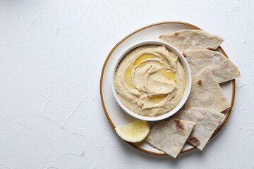 Delicious hummus with olive oil in bowl and pita on light textured table, top view. Space for text