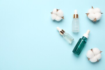 Different cosmetic products and cotton flowers on light blue background, flat lay. Space for text