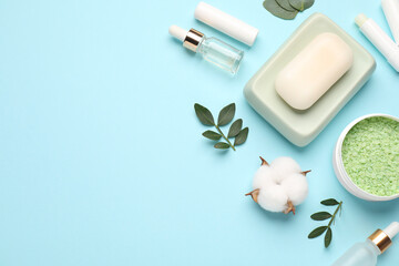 Different cosmetic products, leaves and cotton flower on light blue background, flat lay. Space for text