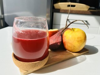 A glass of beetroot mix with apple juice on a wooden board with fresh fruits on the table