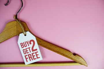 Buy 2 Get 2 Free on price tag with wooden clothes hanger top view on pink background