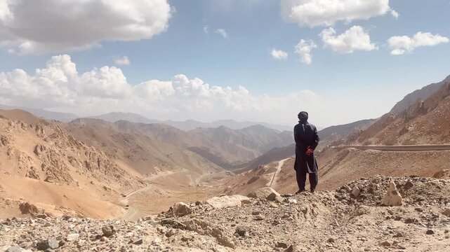 Muslim man stand thoughtful on viewpoint enjoy scenic view in Afghanistan. Salang pass serpentine road scenery. Primary mountain pass connecting northern Afghanistan with Parwan Province