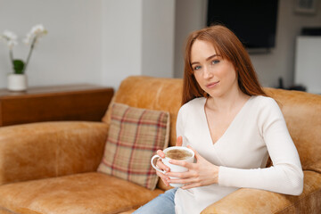 Young Woman Sipping Coffee On A Leather Sofa In A Living Room