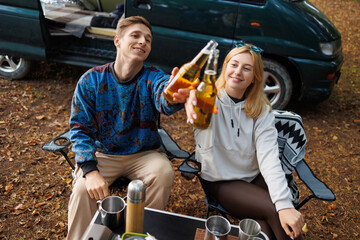 Obraz premium Young Couple Enjoying a Serene Nature Break with Minivan and Beer