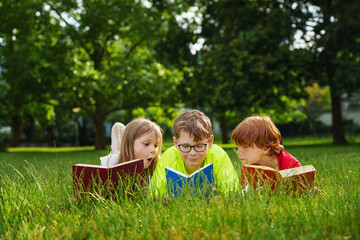 Cute children reading colorful books together outside in the park.