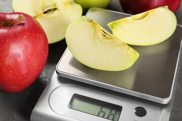 Kitchen scale with pieces of apple and fruits on grey textured table, closeup