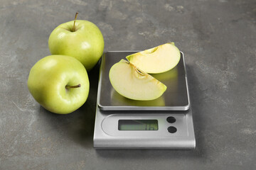 Kitchen scale with pieces of apple and fruits on grey textured table
