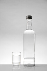Bottle and glass with vodka on white table against light background