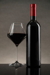 Bottle and glass with red wine on table against gray background