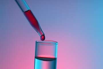 Dripping liquid from pipette into test tube on color background, closeup. Space for text