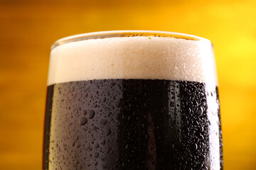 Glass of beer with froth on yellow background, closeup