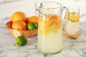 Refreshing lemonade with orange and lime in jug on white marble table