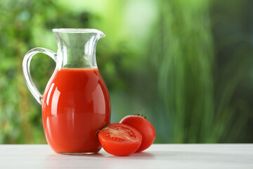 Tasty tomato juice in glass jug and fresh vegetables on white wooden table outdoors, space for text