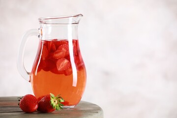 Tasty strawberry lemonade in jug and berries on wooden table against light background, closeup. Space for text