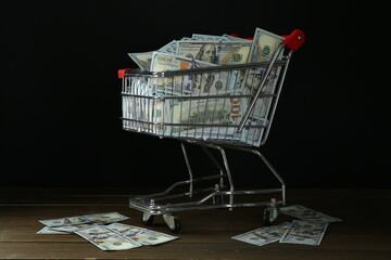 Many dollar banknotes in shopping cart on wooden table