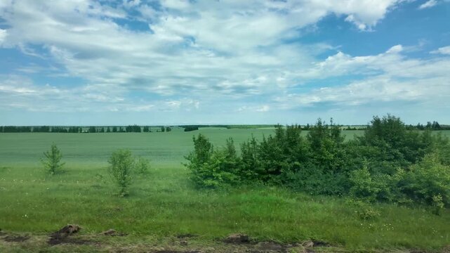 View from the window of endless fields, blue sky with clouds, train travel