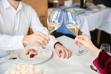 Cropped photo of couple clinking glasses of white wine in the restaurant