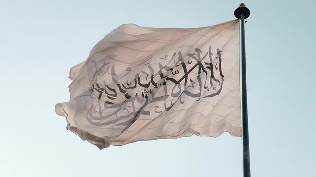 Close up Taliban flag wave with sky background. Islamic Emirate of Afghanistan plain white flag with black words the shahada in center